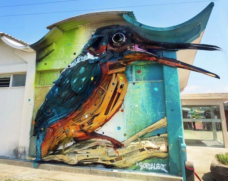 a colorful bird painted on the side of a building in front of a white house