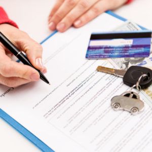 a person holding a pen over a document with keys and money