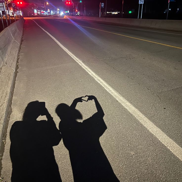 two people standing in the middle of an empty street at night with their shadows on the ground