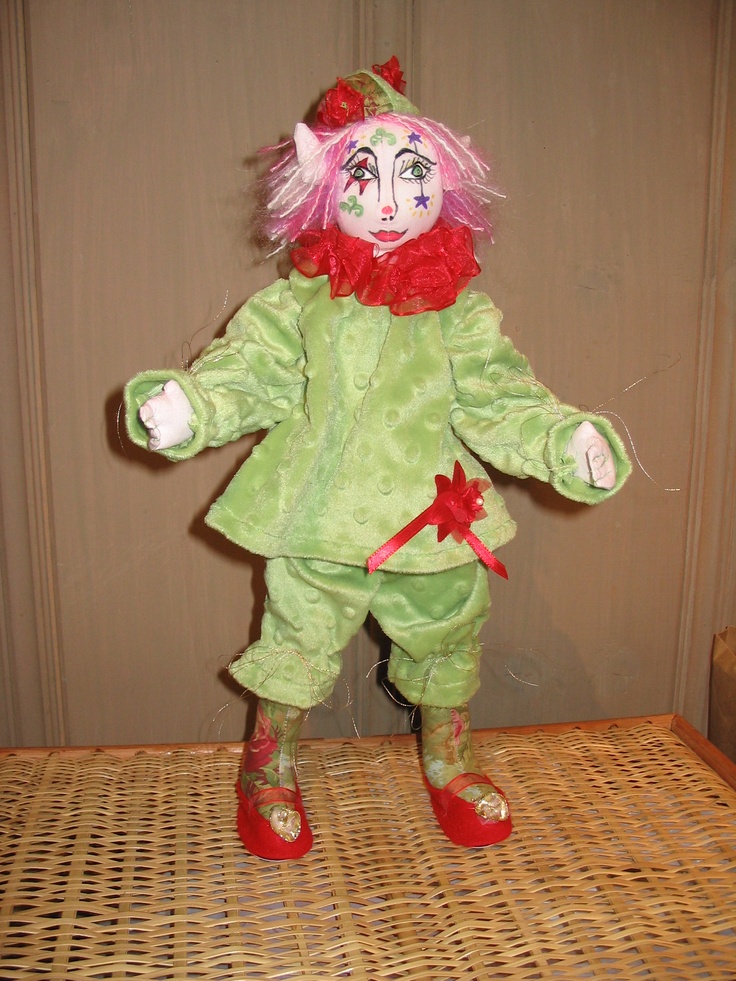 a green doll with pink hair standing on a wicker floor next to a wall