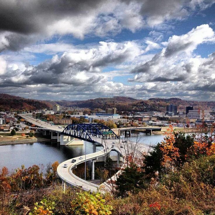 a view of a bridge over a body of water with fall foliage around it and clouds in the sky