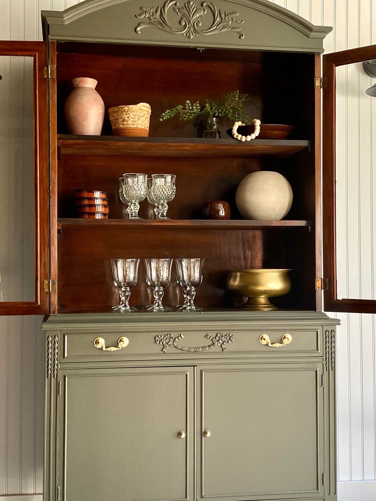 an antique china cabinet with wine glasses and vases on it's top shelf