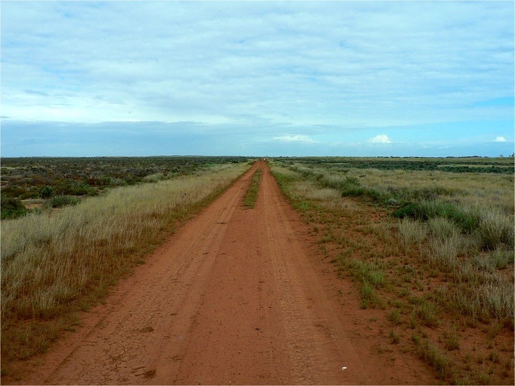 an empty dirt road with grass on both sides and blue sky in the back ground