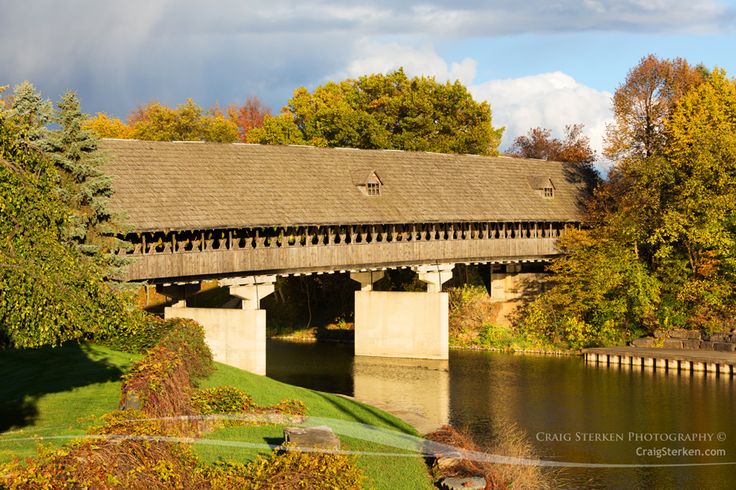 an old covered bridge over a body of water in the fall with trees around it