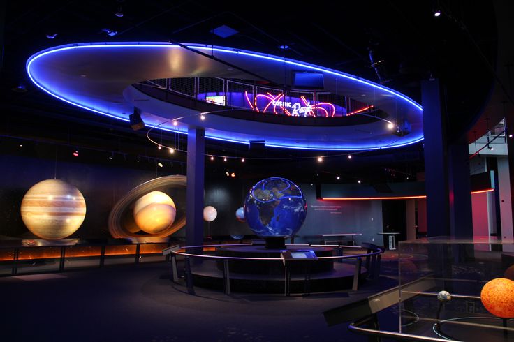 an image of a museum setting with planets in the center and lights on display behind it