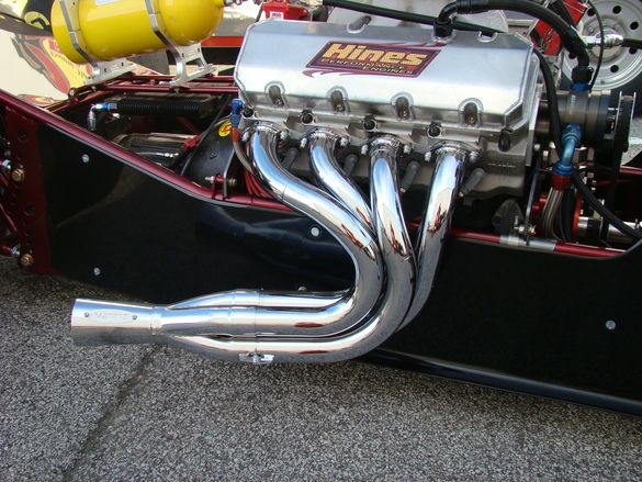 the engine compartment of a race car with chrome exhaust pipes and an aluminum radiator