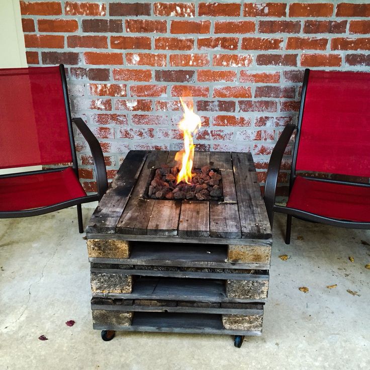 a fire pit made out of pallets with red chairs around it and brick wall in the background