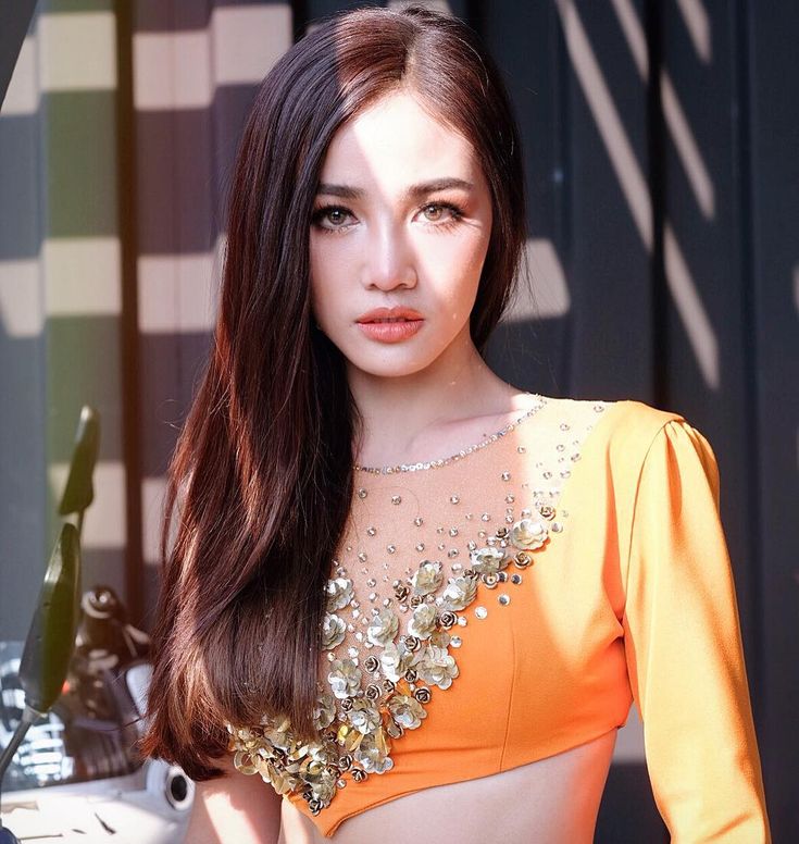 a woman with long brown hair wearing an orange top and posing for a photo in front of a building