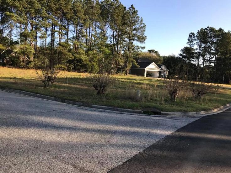 an empty street in the middle of a wooded area with a small white house behind it