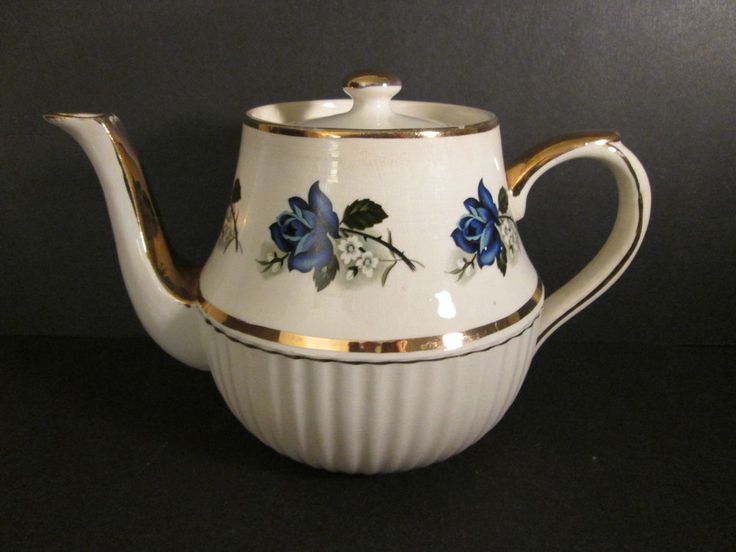 a white tea pot with blue flowers painted on the side and gold trimmings