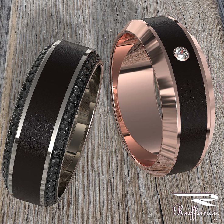 two wedding bands with black diamonds are shown on a wooden surface and one has a diamond in the center