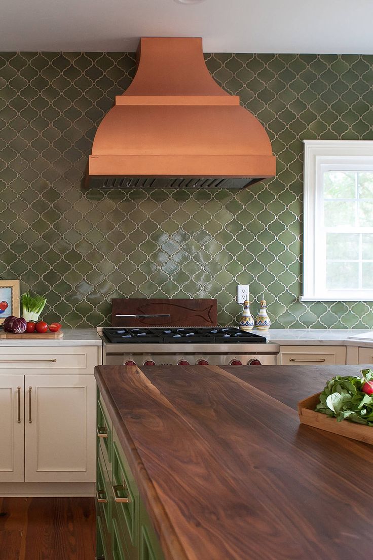 a kitchen with green tile and wooden counter tops, an island in the middle has vegetables on it