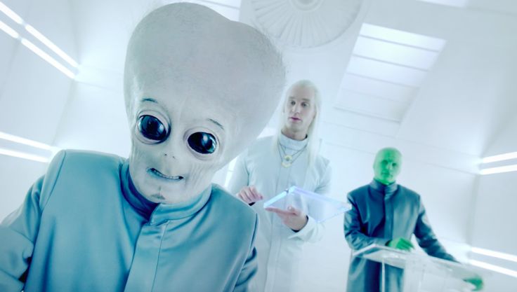 two people standing next to each other in a room with aliens on the floor and one person wearing an alien suit