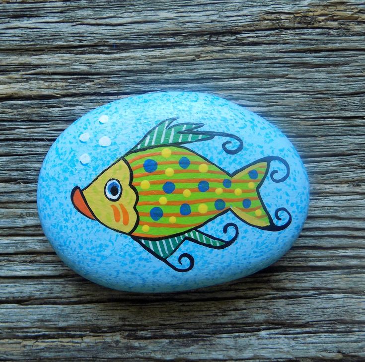 a painted rock with a fish on it sitting on top of a wooden planks