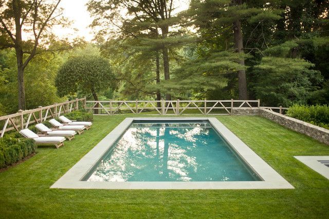 an empty pool surrounded by lawn chairs in the middle of a lush green yard with trees