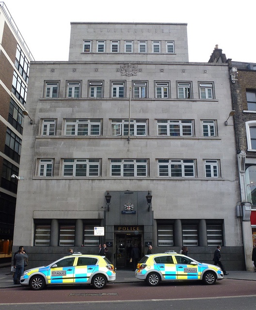 two police cars are parked in front of a large building with multiple stories and windows