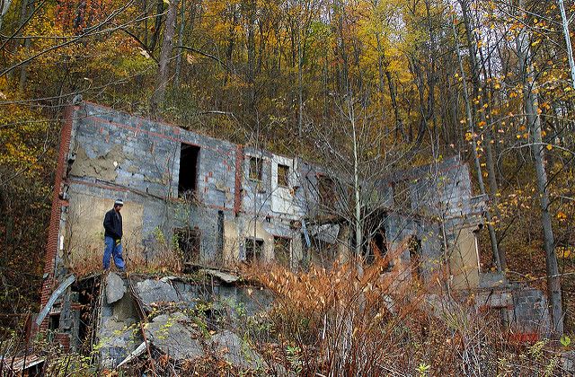 a man standing in front of an old run down building surrounded by trees and foliage