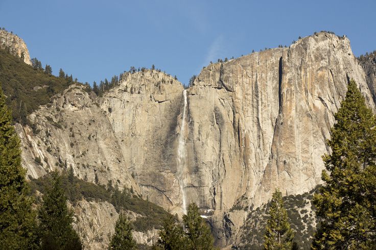 the top of a tall mountain with trees around it and a waterfall in the distance