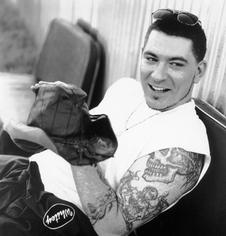 a black and white photo of a man with tattoos on his arm holding a pair of shoes