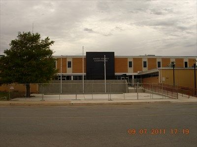 an empty parking lot in front of a building with a fence around it and trees on the other side