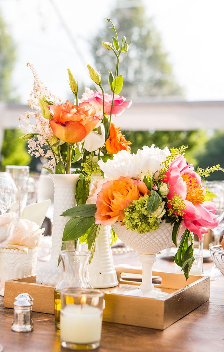 a wooden table topped with white vases filled with different types of flowers and greenery