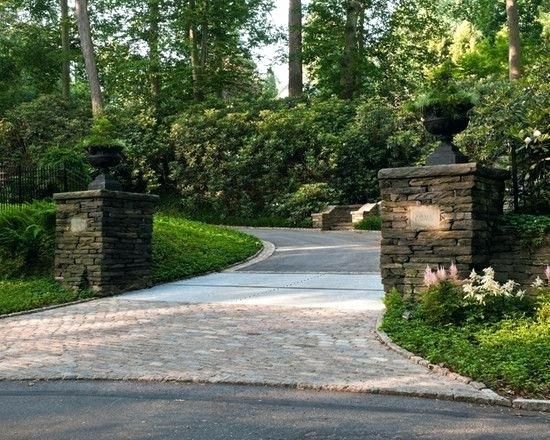 a driveway entrance with stone pillars and landscaping