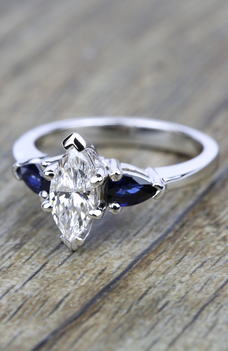 an oval cut diamond and blue sapphire engagement ring on a wooden table with wood grain background