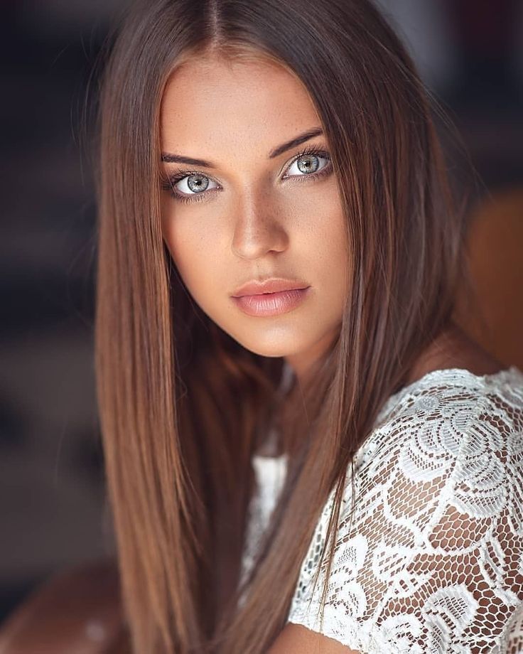 a woman with long brown hair and blue eyes is looking at the camera while wearing a white top