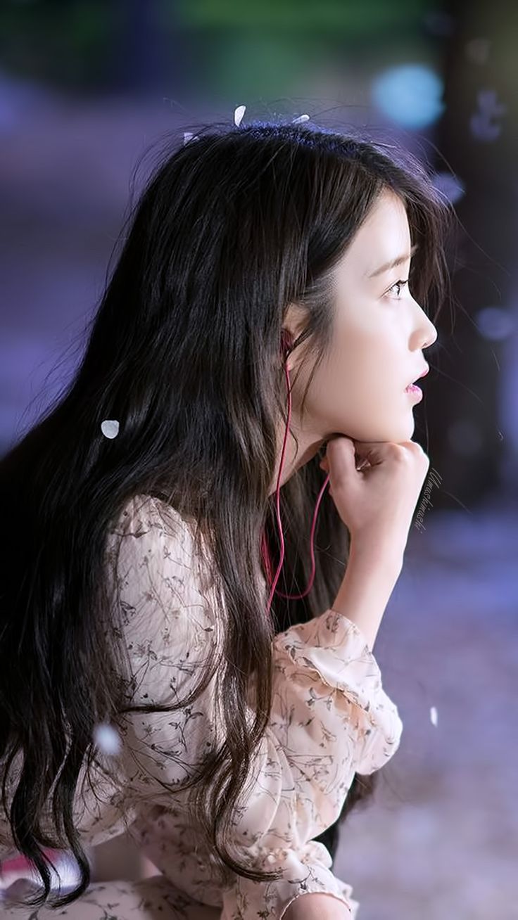 a woman with long hair sitting on the ground and listening to her earphones while looking off into the distance