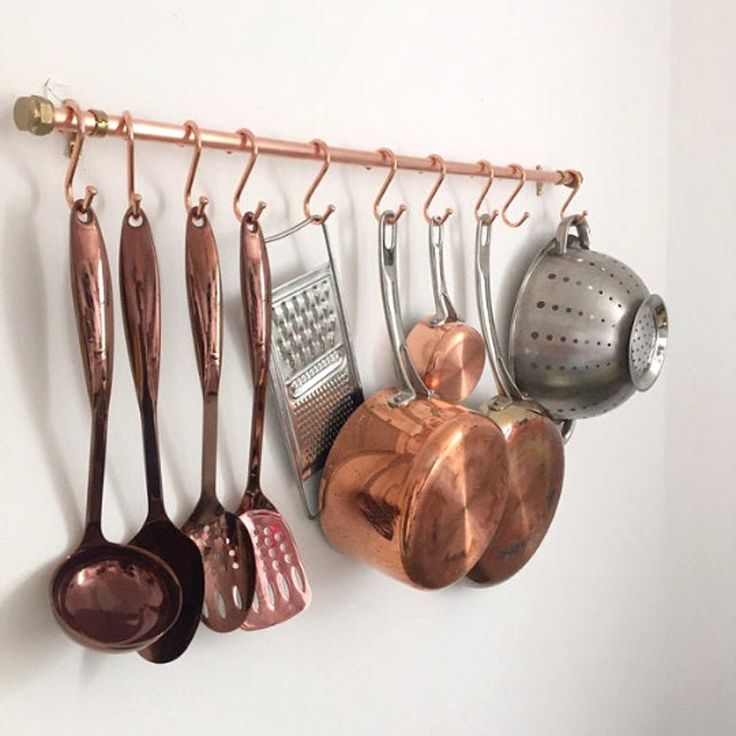 copper pots and pans are hanging on the wall next to utensils,