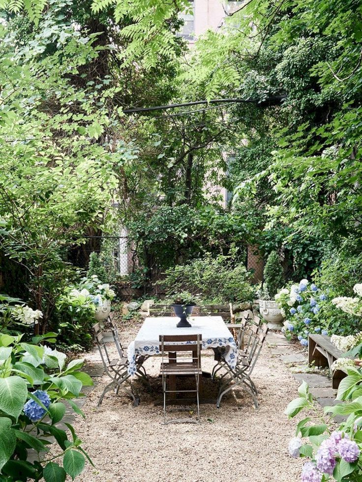 an outdoor table and chairs in the middle of a garden with lots of greenery