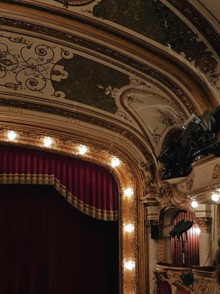 an ornately decorated auditorium with red curtains and lights on the ceiling, in front of a stage