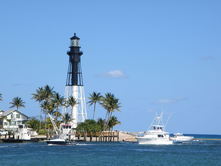 a light house sitting on top of a lush green field next to the ocean and palm trees