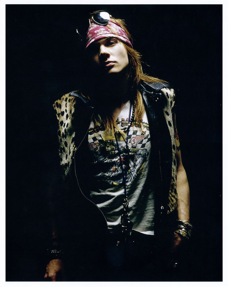 a man with long hair wearing a bandana and leather vest standing in the dark