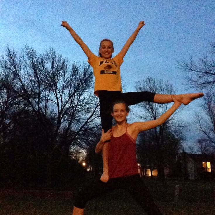 two people are doing acrobatic tricks in the park at night with their hands up