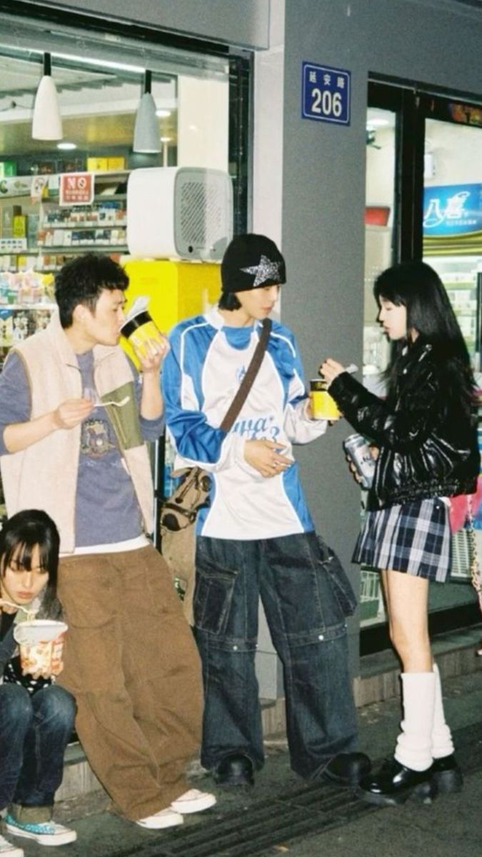 four people standing on the sidewalk eating ice cream and talking to each other in front of a convenience store