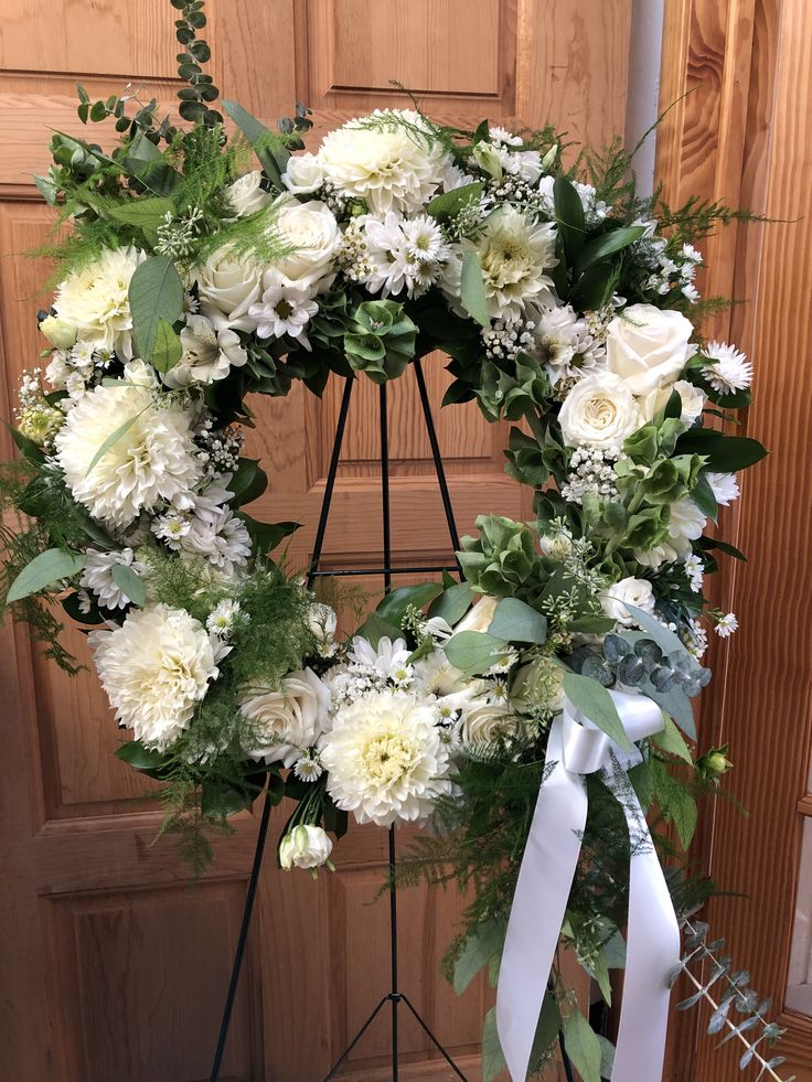 a wreath with white flowers and greenery in front of a wooden door