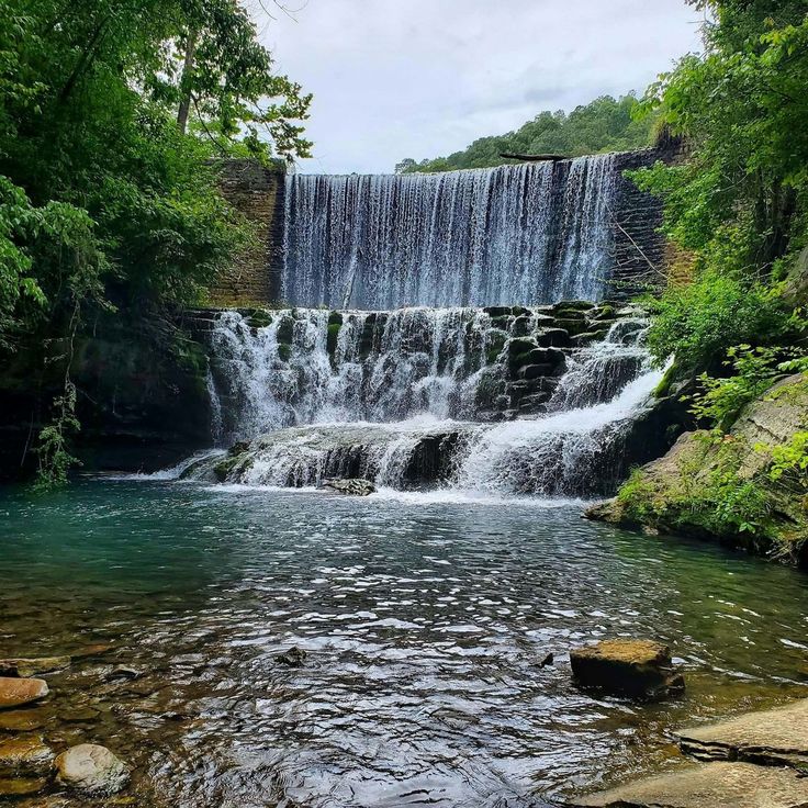 a waterfall with water running over rocks in the foreground and trees on either side