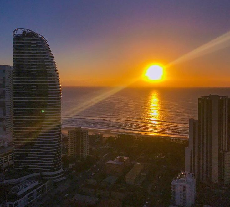 the sun is setting over the ocean and buildings in the foreground, as seen from a high rise building