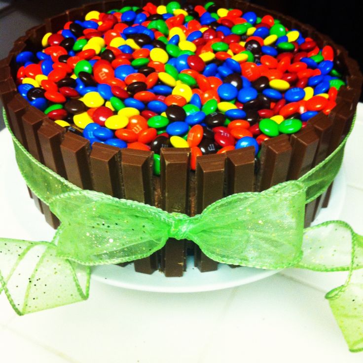 a chocolate cake with colorful candy toppings and green bow on the top, sitting on a white plate