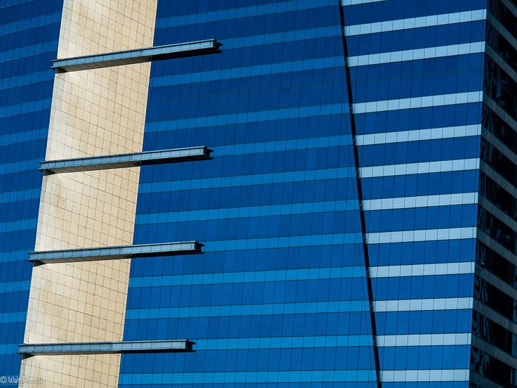 an airplane is flying in front of a tall building with blue glass on it's side