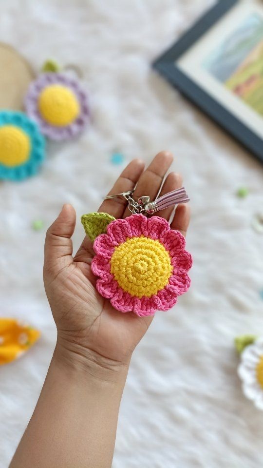 a hand holding a crocheted flower keychain in the shape of a sunflower