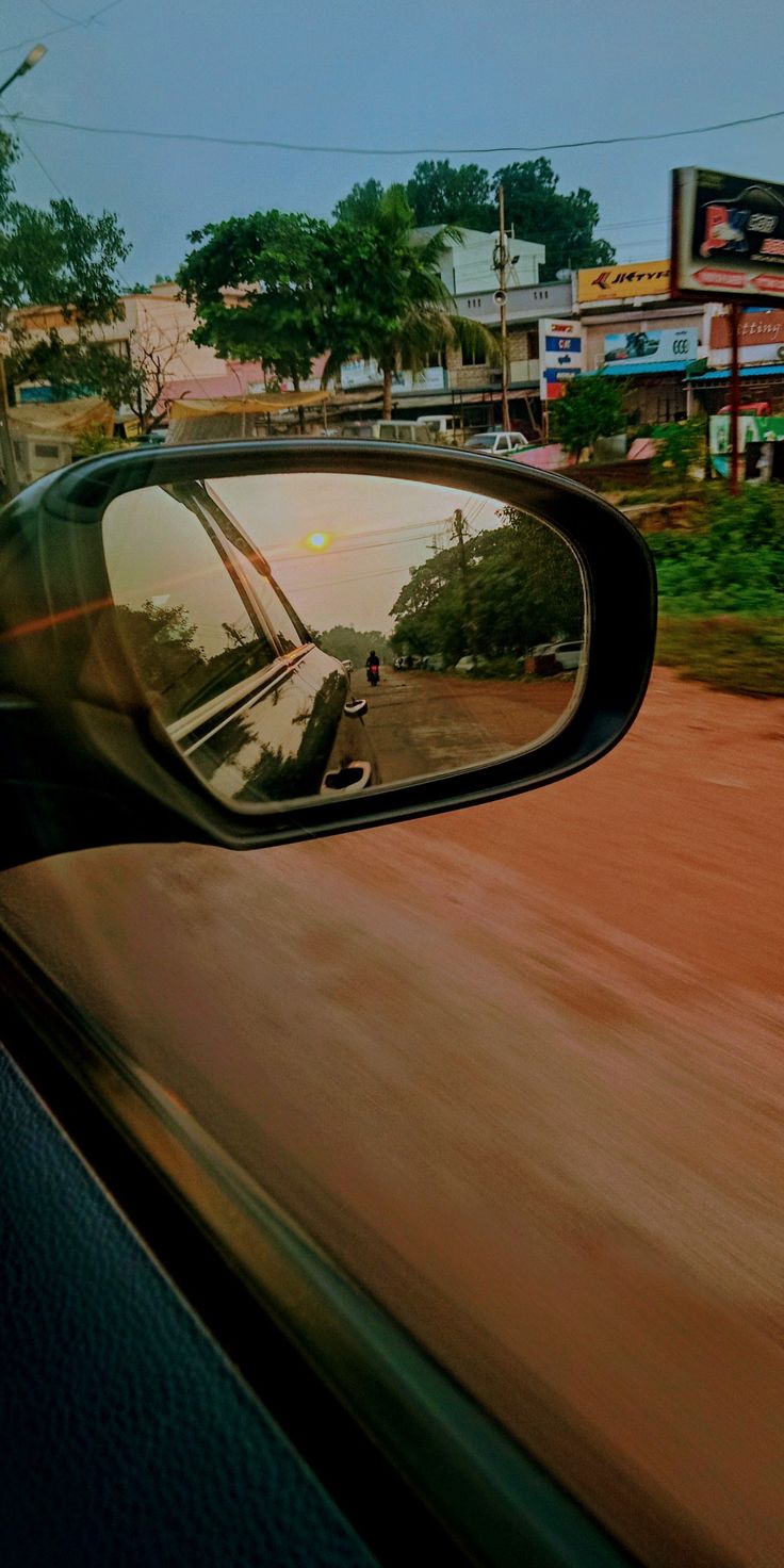 a car's side view mirror is shown as it drives down the road in front of some buildings