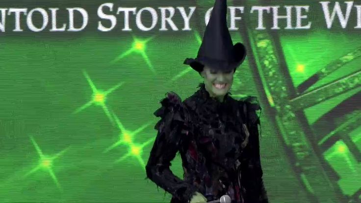 a woman in a witches costume on stage with a green background and the words unto story of the witch