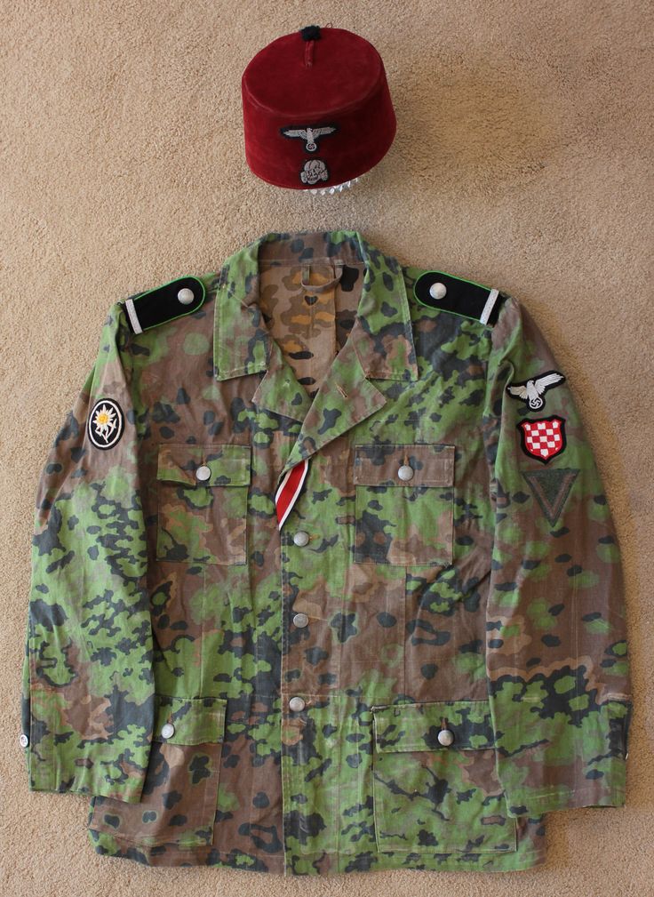 a camouflage jacket and hat are laying on the floor next to each other, including a red cap