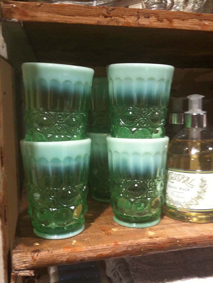 four green glasses sitting on top of a wooden shelf