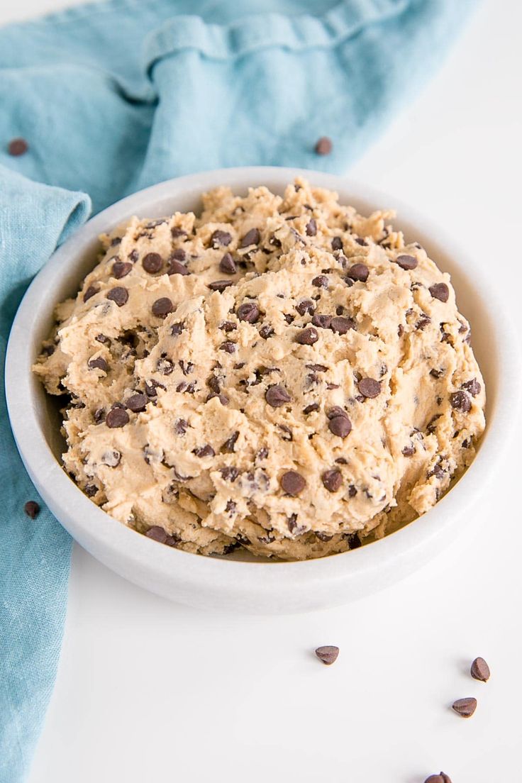 a bowl filled with cookie dough on top of a blue napkin next to chocolate chips