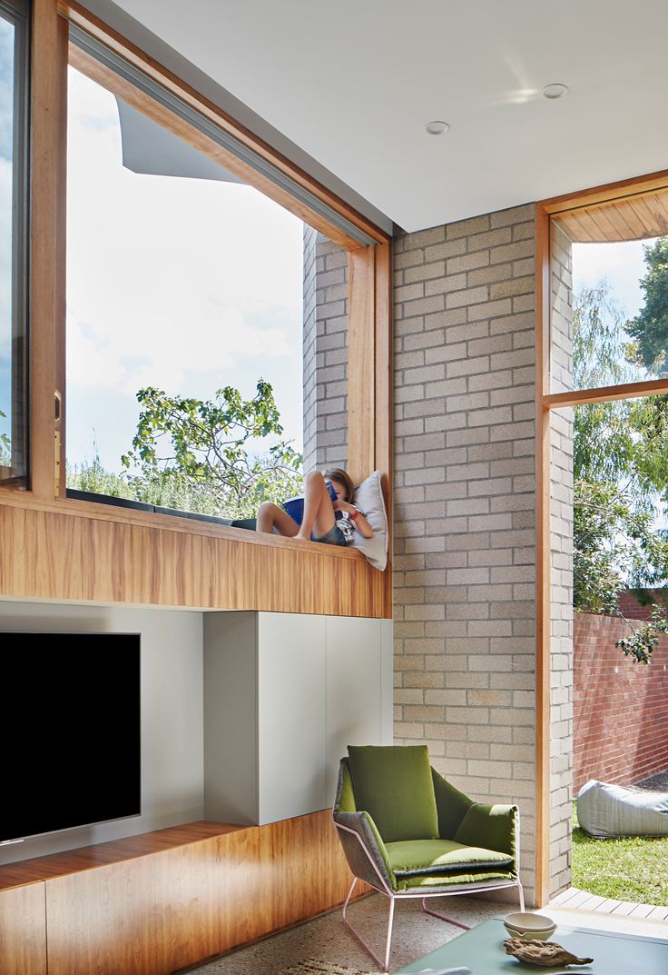 a woman laying on top of a window sill in a living room next to a green chair