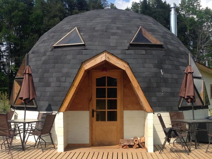 a round building with an open door and wooden flooring on the outside, surrounded by lawn chairs and umbrellas