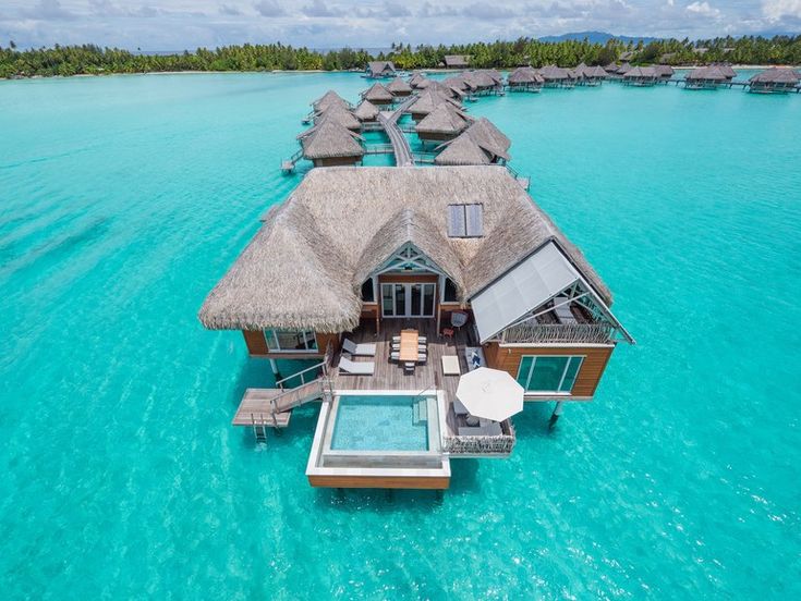 an aerial view of a house on the water with thatched roof and swimming pool